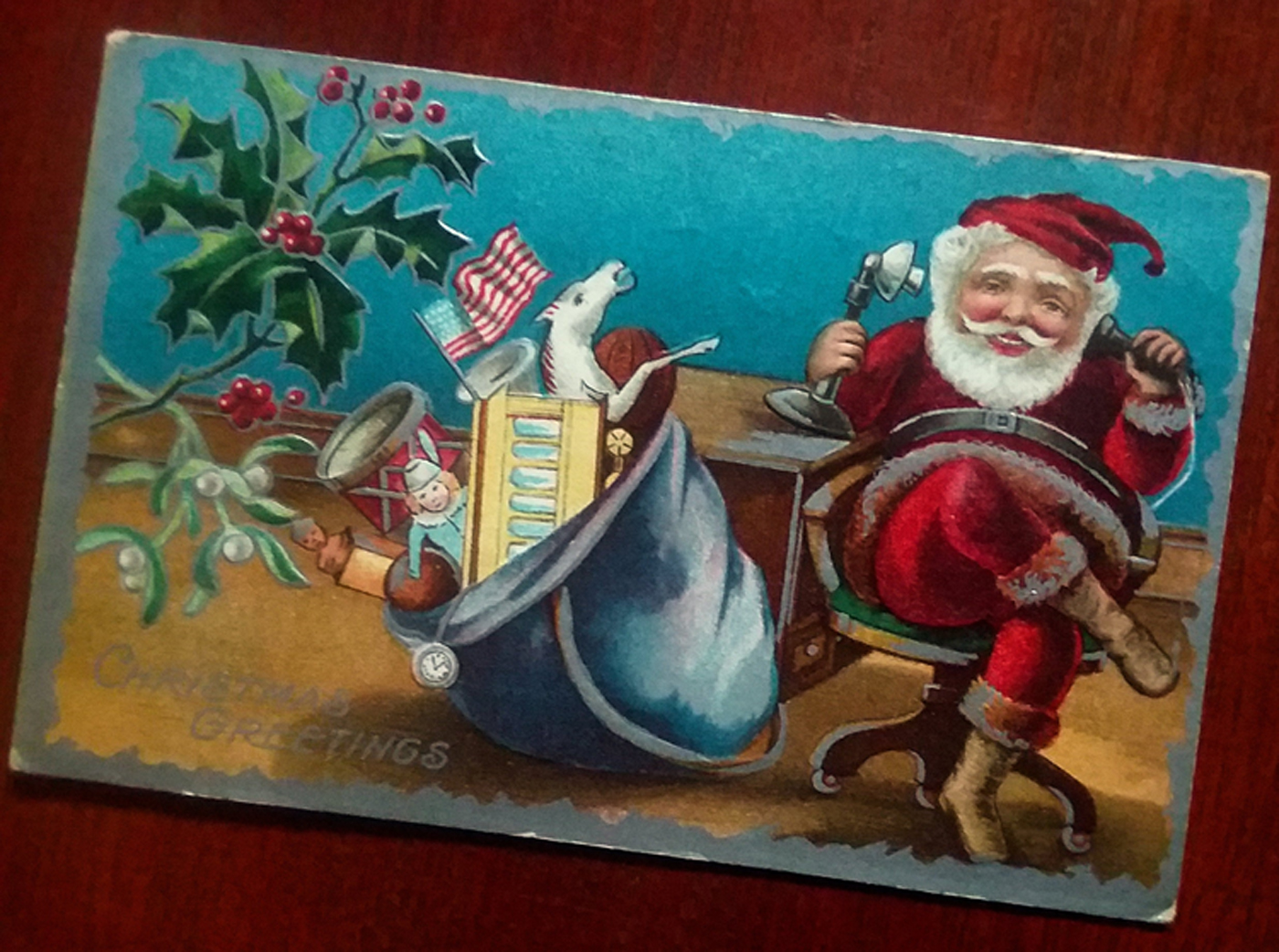 Santa chatting on an old-fashioned telephone with his sack of toys beside him.